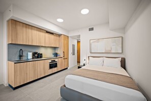Una habitación de hotel moderna con kitchenette, una cama y un ventanal grande.