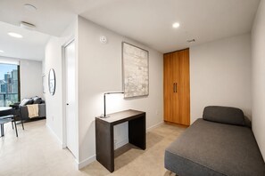 Ein modernes Schlafzimmer mit Bett, Schreibtisch mit Lampe, Kleiderschrank und Blick auf die Stadt durch ein Fenster.