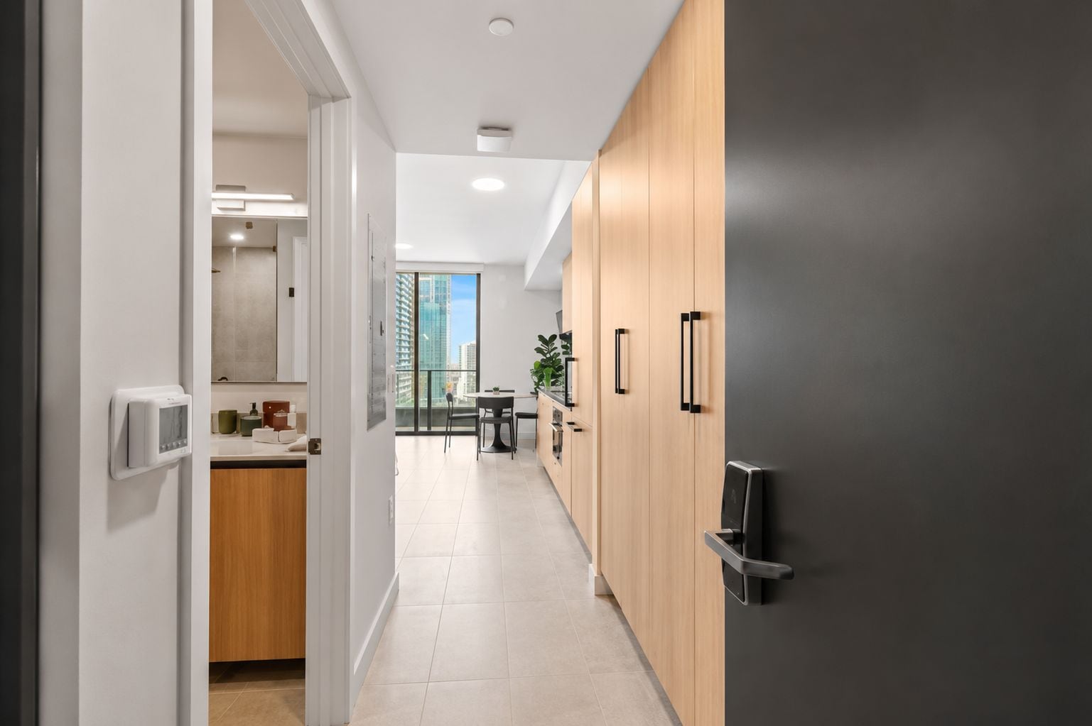 Una cocina moderna con armarios de madera, un refrigerador negro y vistas a un balcón con un paisaje urbano.