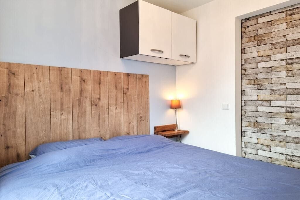 Un dormitorio con cabecera de madera, cama con colcha azul, mesita de noche con lámpara y pared con diseño de ladrillo.