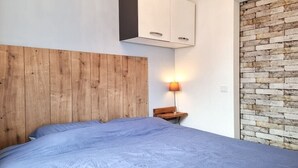 Quarto com cabeceira de madeira, cama com colcha azul, mesa de cabeceira com abajur e parede com padrão de tijolos.
