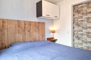 Ein Schlafzimmer mit einem hölzernen Kopfteil, einem Bett mit blauer Bettdecke, einem Nachttisch mit Lampe und einer Wand mit Backsteinmuster.