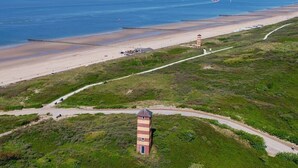 Paisagem costeira com um farol, uma praia e uma estrada que leva ao farol.