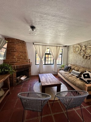 A cozy living room with a brick fireplace, a sofa, two wicker chairs, and a coffee table. - Mazamitla Villas Buenos Aires (Mazamitla)