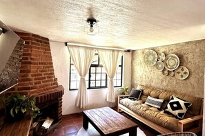 A cozy living room with a brick fireplace, a wooden coffee table, a sofa with cushions, and a wall with decorative plates. - Mazamitla Villas Buenos Aires (Mazamitla)