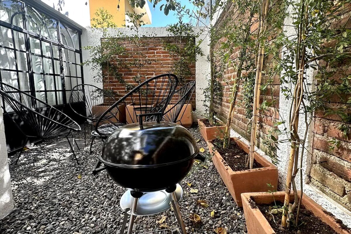 A barbecue grill in a garden area with a brick wall and potted plants.