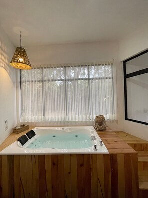 Un baño moderno con tocador de madera, bañera independiente y un gran ventanal con cortinas traslúcidas.
