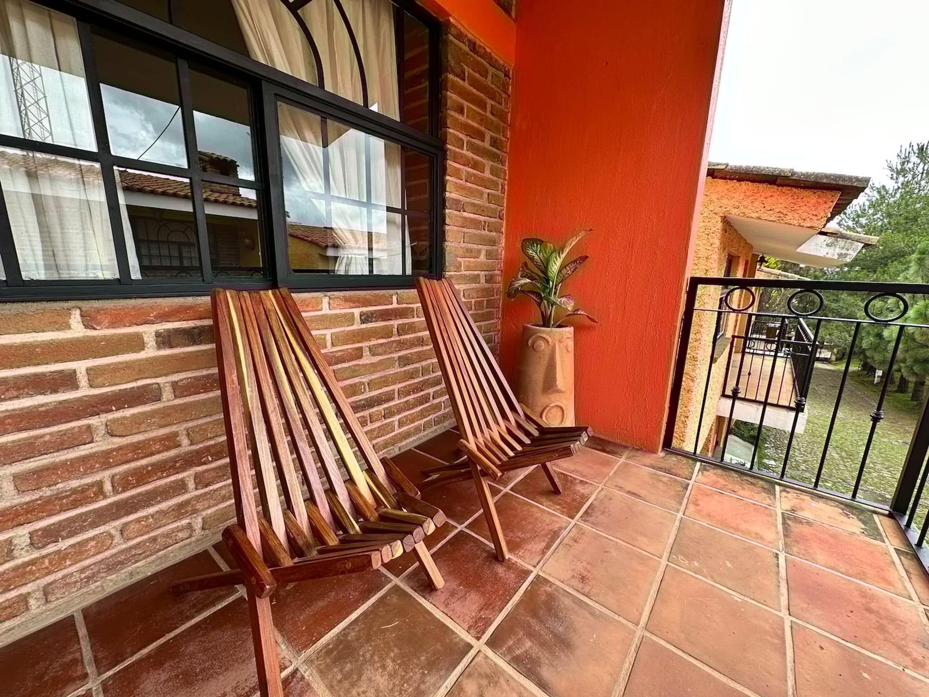 Un balcón con dos sillas de madera, una planta en maceta y vistas a un jardín.