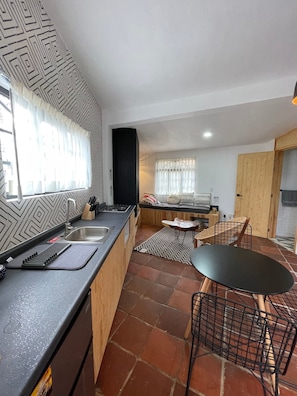 A modern kitchen with a black countertop, stainless steel sink, and a black chair.