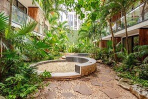 Ein Innenhof mit einem kreisförmigen Wasserspiel, umgeben von üppiger Vegetation und einem Steinweg.