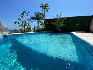 A clear blue swimming pool with a tiled edge, surrounded by greenery and a hedge. - The Shore PDC (Playa del Carmen)