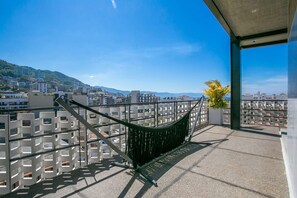 Ein Balkon mit einer Hängematte, Blick auf eine Stadtlandschaft und ein Berg in der Ferne.