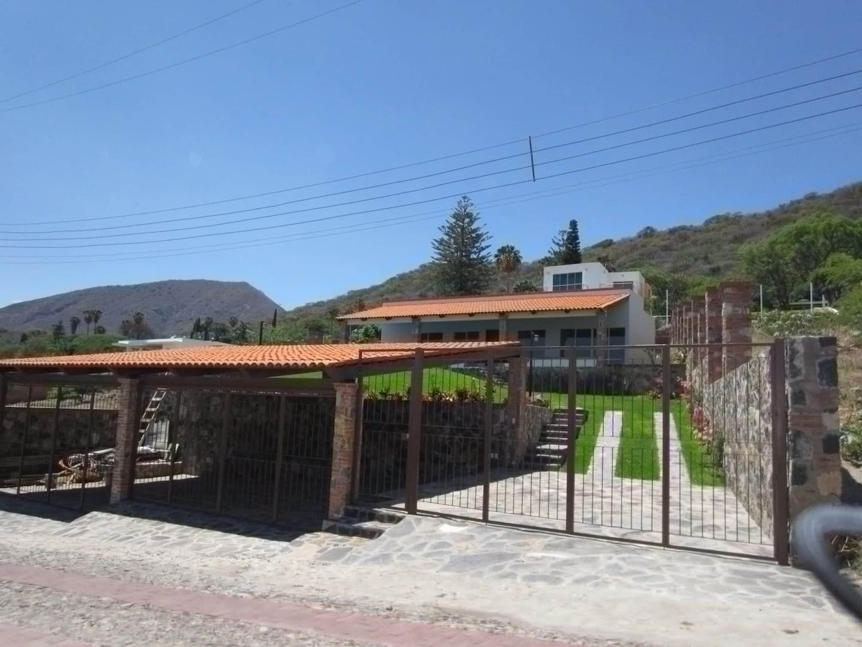 Una propiedad cerrada con entrada pavimentada, un área techada y un edificio con techo de tejas rojas.