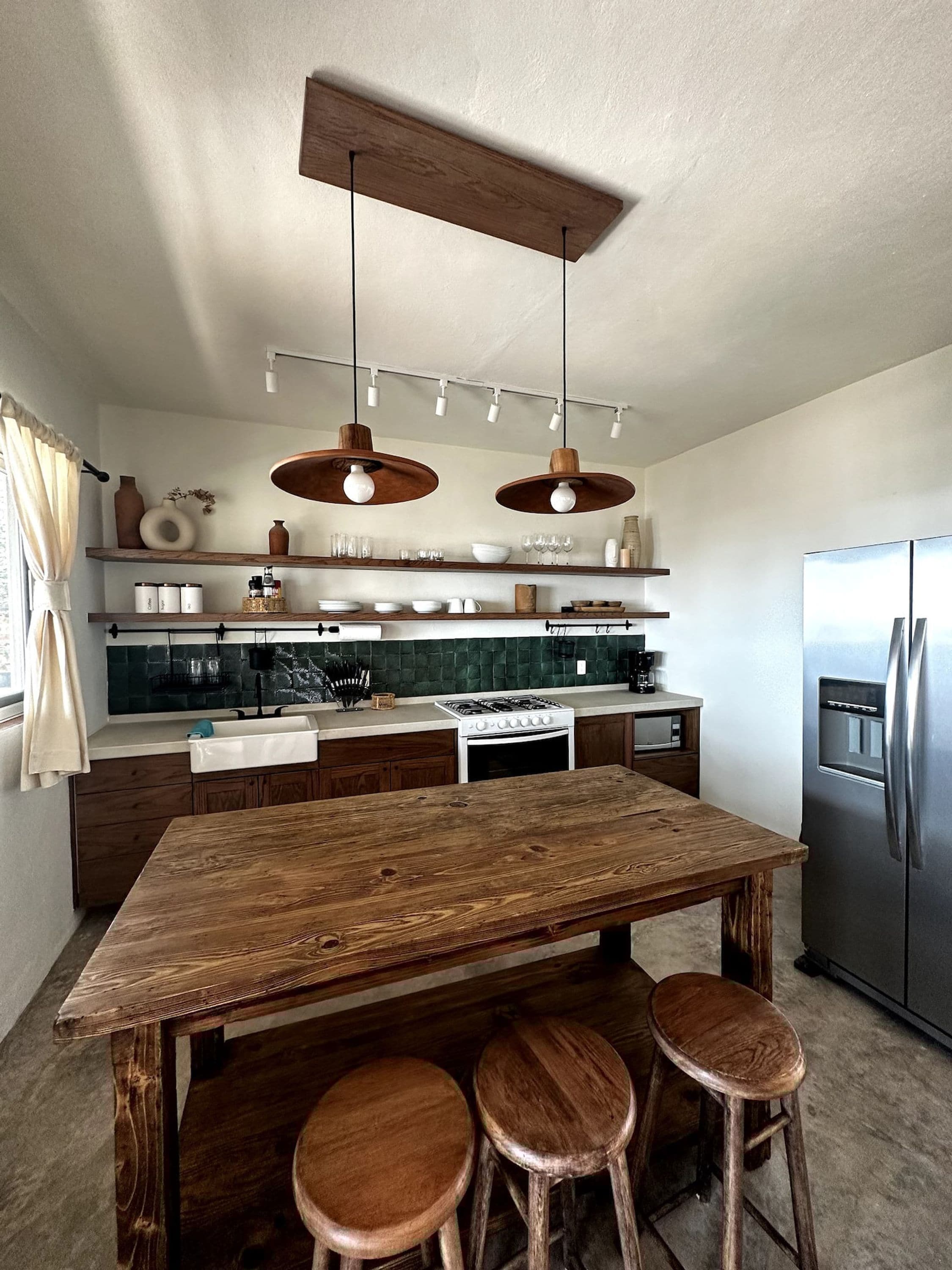 Una cocina moderna con una isla de madera, taburetes de bar, un refrigerador de acero inoxidable e iluminación colgante.