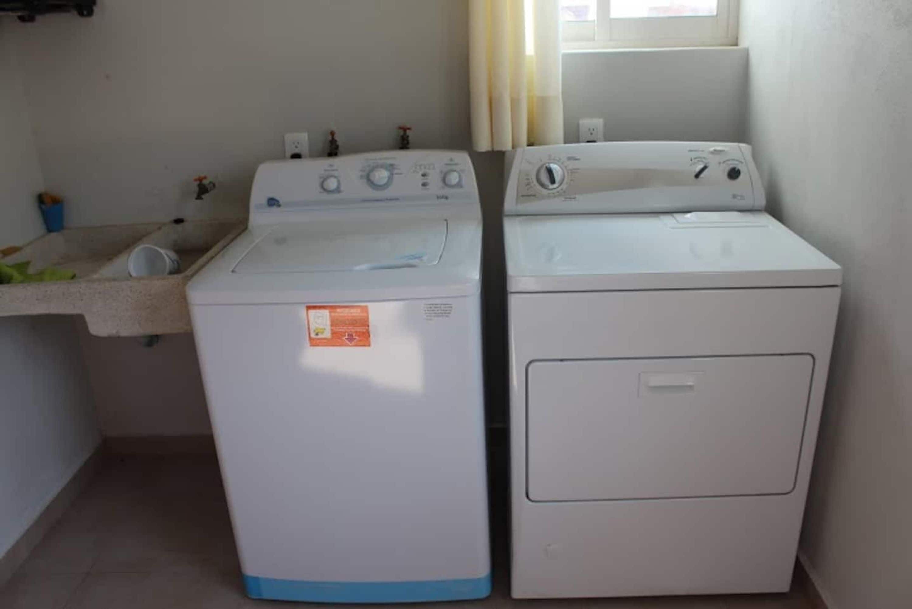Zona de lavandería con dos lavadoras blancas y una encimera con lavabo.