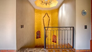 Un couloir avec un mur jaune, un lustre, une grille en métal et un sol carrelé.