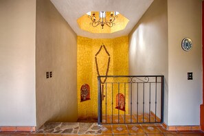 A hallway with a yellow wall, a chandelier, a metal gate, and a tiled floor.
