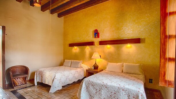 Une chambre avec deux lits, une chaise, une lampe et une petite statue religieuse accrochée au mur.
