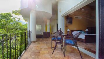 A balcony with a table and chairs, a sofa, and a bed with a TV.