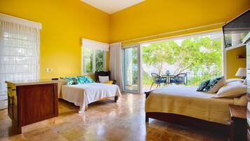 A hotel room with two beds, a dining area, and a view of greenery outside.