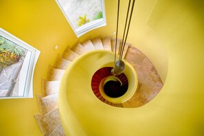 A spiral staircase with a yellow wall and a window with a view of plants. - Amazing View to los Arcos -4 Bedroom Villa (Puerto Vallarta)