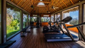 A gym with exercise equipment, large windows, and a thatched roof.