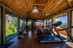 A gym with exercise equipment, large windows, and a thatched roof.