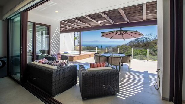 A modern outdoor living space with wicker furniture, a table, and an umbrella, overlooking a scenic view.