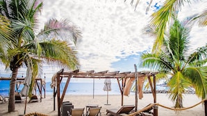 A beach with a wooden pergola, lounge chairs, and a rope barrier.