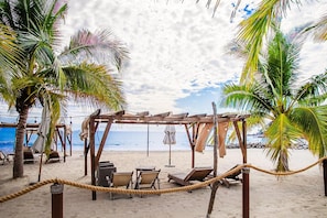 A beach with a wooden pergola, lounge chairs, and a rope barrier.