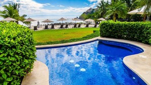 A swimming pool with a curved design, surrounded by greenery and lounge chairs.