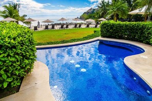 A swimming pool with a curved design, surrounded by greenery and lounge chairs.