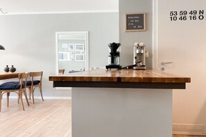 Uma área de cozinha com bancada de madeira, máquina de café e placa na parede com coordenadas.