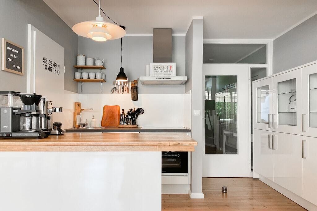A modern kitchen with a wooden countertop, a coffee machine, and a hanging light fixture.