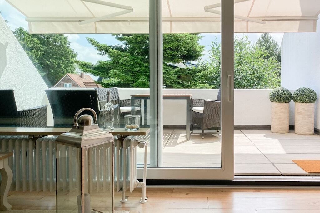 A modern outdoor patio with a glass door leading to a garden, furnished with wicker chairs and a table.