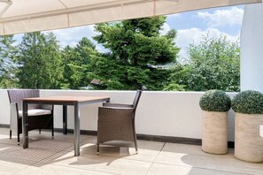 Eine Terrasse mit Tisch und Stühlen, zwei Kübelpflanzen und Blick auf Bäume und Gebäude.