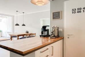 Cozinha com bancada de madeira, máquina de café e luminária pendente.