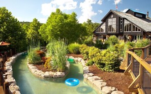 A landscaped garden with a water feature, a wooden deck, and a building with a stone facade. - Big Cedar | Family Lake Escape | Pool & Nature | 2BR Lodge (Ridgedale)