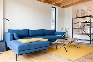 A modern living room with a blue sofa, a wooden coffee table, and a black shelving unit. - Holiday apartment with 2 bedrooms (Scharbeutz)