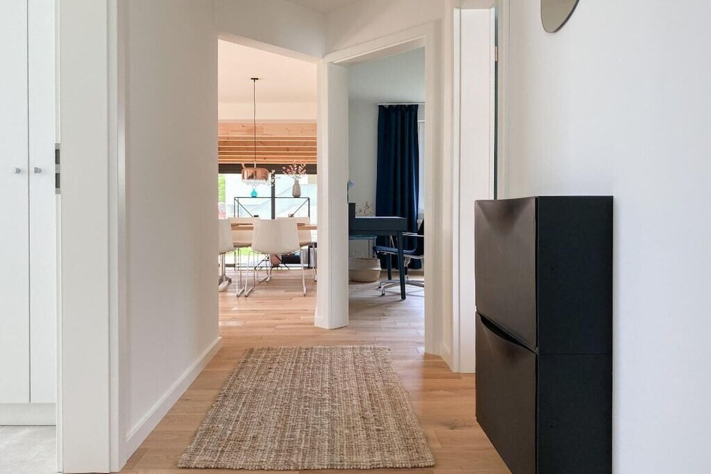 A hallway with a rug leading to a dining area with a table and chairs, a black refrigerator, and a ceiling light fixture.