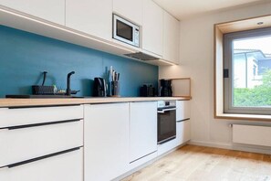 A modern kitchen with white cabinetry, a blue accent wall, and a window providing natural light. - Holiday apartment with 2 bedrooms (Scharbeutz)