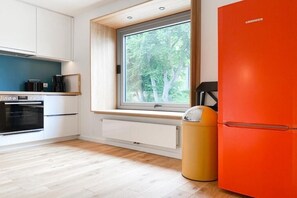 Une cuisine moderne avec une fenêtre, des meubles blancs, un four noir et un réfrigérateur orange vif.