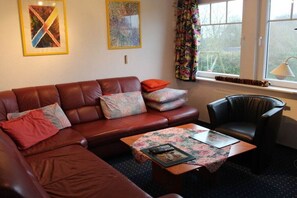 Ein Wohnzimmer mit einem braunen Ledersofa, einem schwarzen Ledersessel und einem kleinen Tisch mit einer Tischdecke mit Blumenmuster.