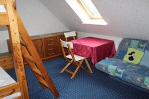 Ein Zimmer mit Etagenbett, Schreibtisch mit Stuhl, kleinem Tisch mit rotem Tischläufer und einer Couch mit bunter Decke.