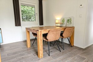 A dining area with a wooden table and two chairs, a window with curtains, and a wall-mounted lamp.