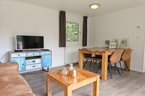 A living room with a television, a wooden dining table with chairs, a sofa, and a small coffee table with decorative items.