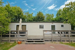 A mobile home with a wooden deck, a covered patio, and a sign indicating a room number.