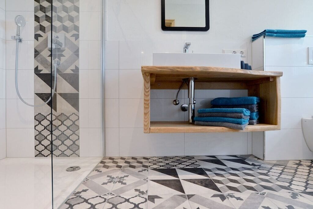 Un bagno con doccia, un lavandino con ripiano in legno e piastrelle decorate.