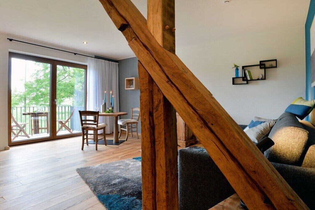 Une pièce dotée d’une structure en poutres apparentes, d’un coin repas avec des chaises et une table, et d’un canapé agrémenté de coussins.