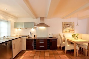 A compact kitchen with a built-in dishwasher, a stove, and a dining area with a table and chairs. - Holiday apartment in Sylt with 2 bedrooms (Keitum)